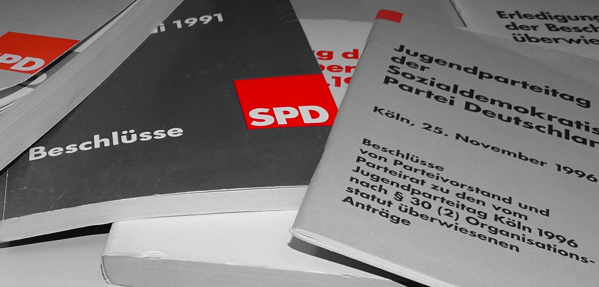 Schwarz-Weiß Foto Bücherstapel mit Beschlüssen der SPD. Logos der SPD auf den Büchern in Rot.