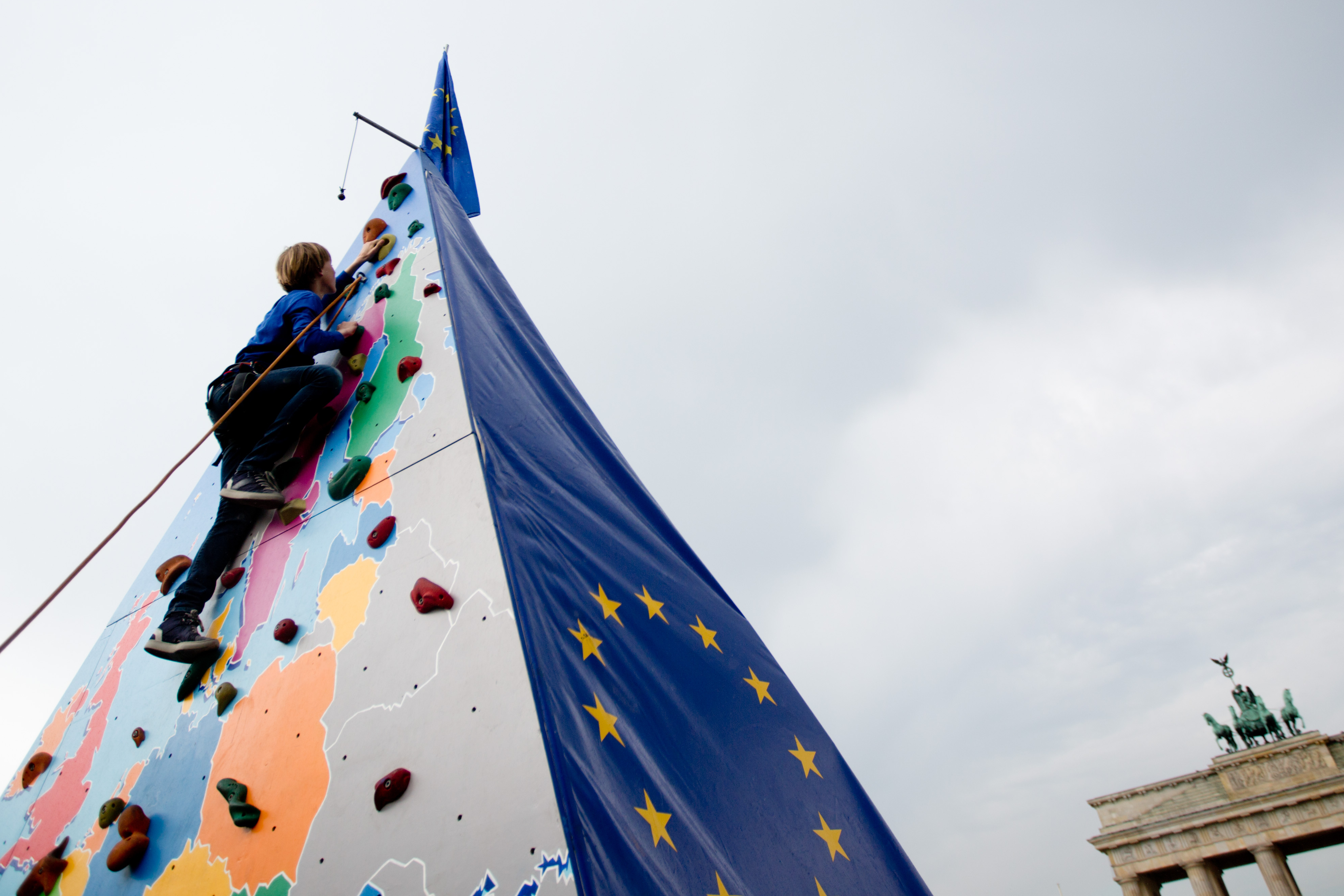 Ein Kind klettert eine Pyramide hoch auf der eine Karte von Europa und die EU-Flagge zu sehen ist. 