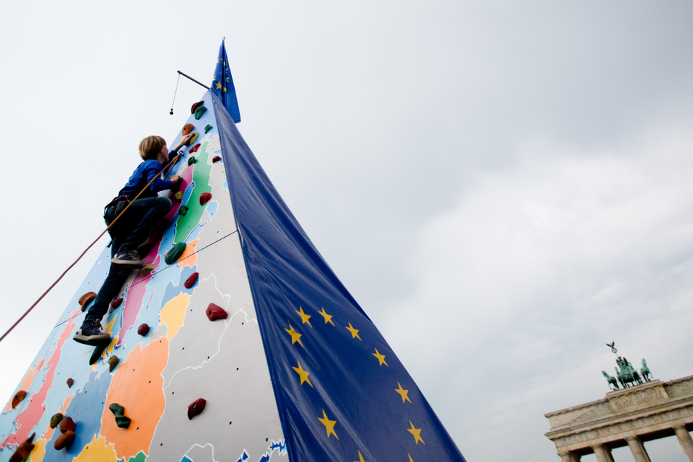 Ein Kind klettert eine Pyramide hoch auf der eine Karte von Europa und die EU-Flagge zu sehen ist. 
