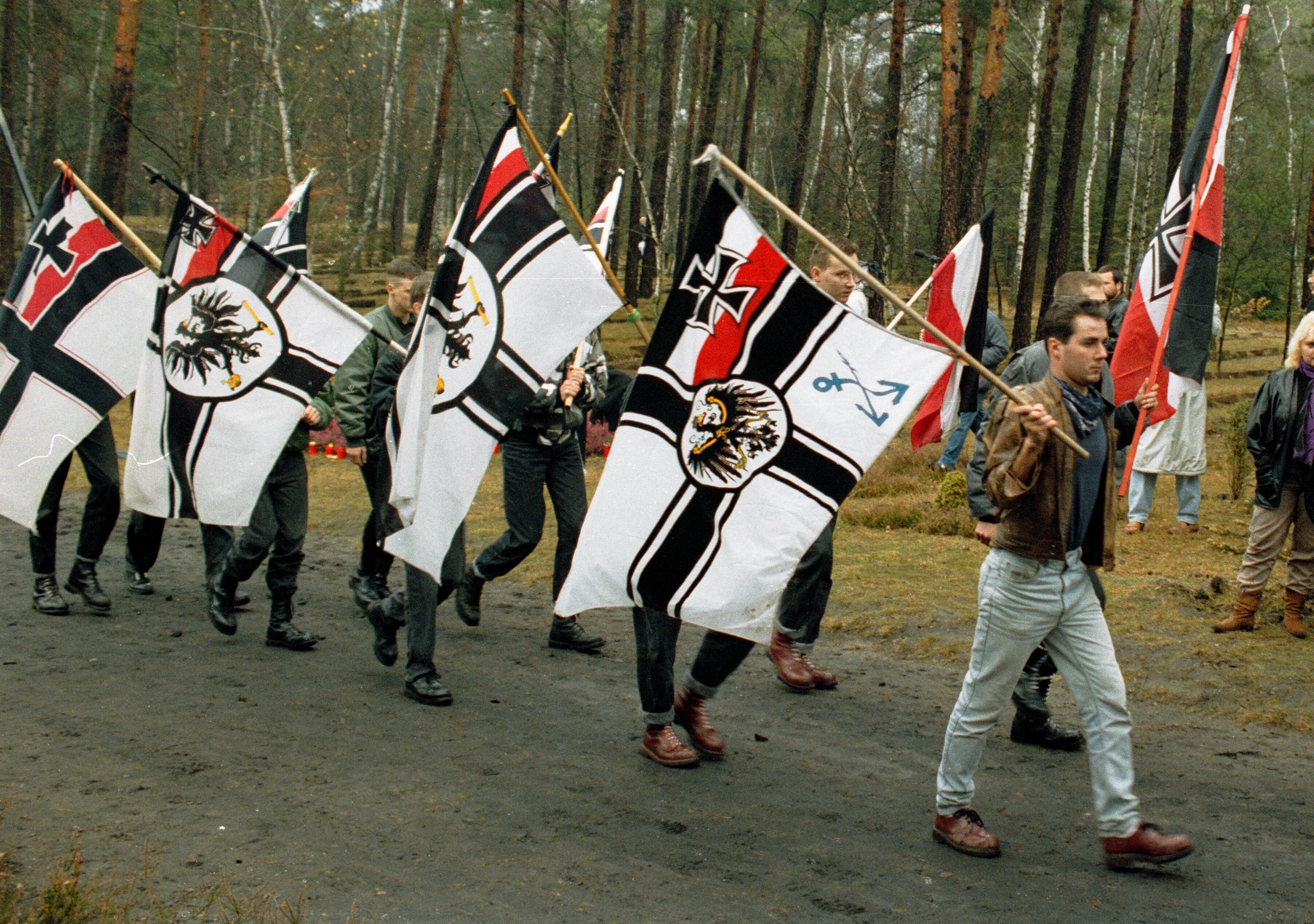 Junge Männer mit Reichskriegsflaggen, die mit einem Demonstrationszug durch den Wald gehen