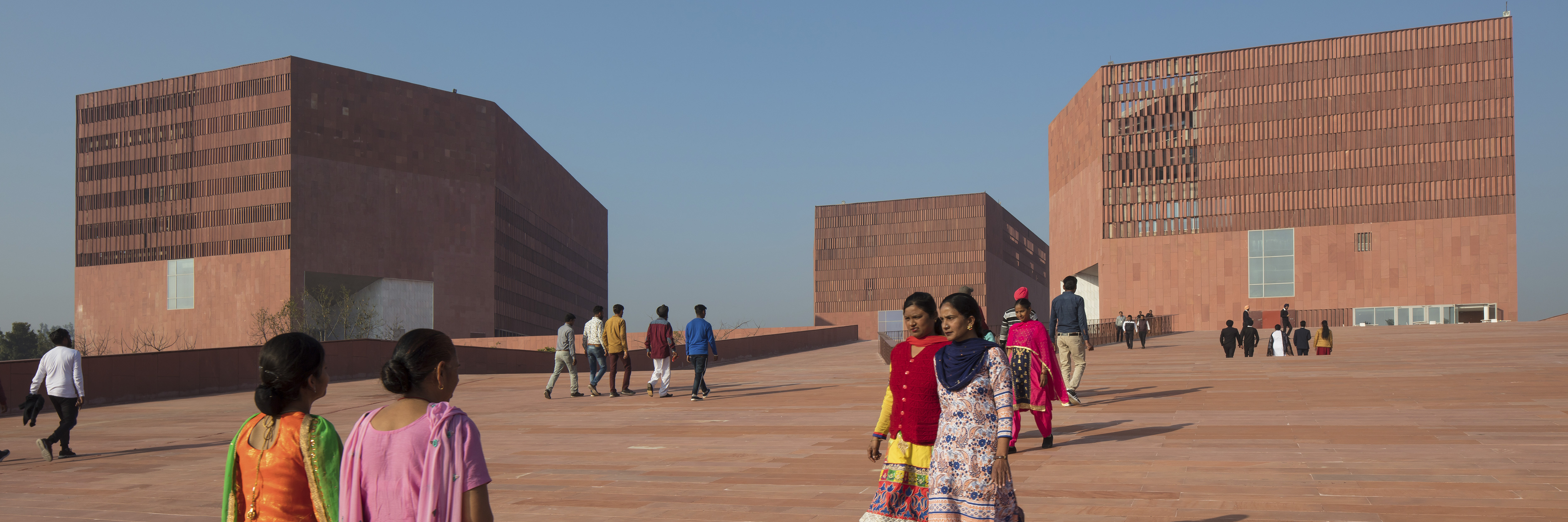 Fußweg auf dem Campus der Thapar University, Patiala, Indien mit Studierenden vor einem sehr modernen Gebäude des Architekten McCullough Mulvin Architects vor blauem Himmel. 