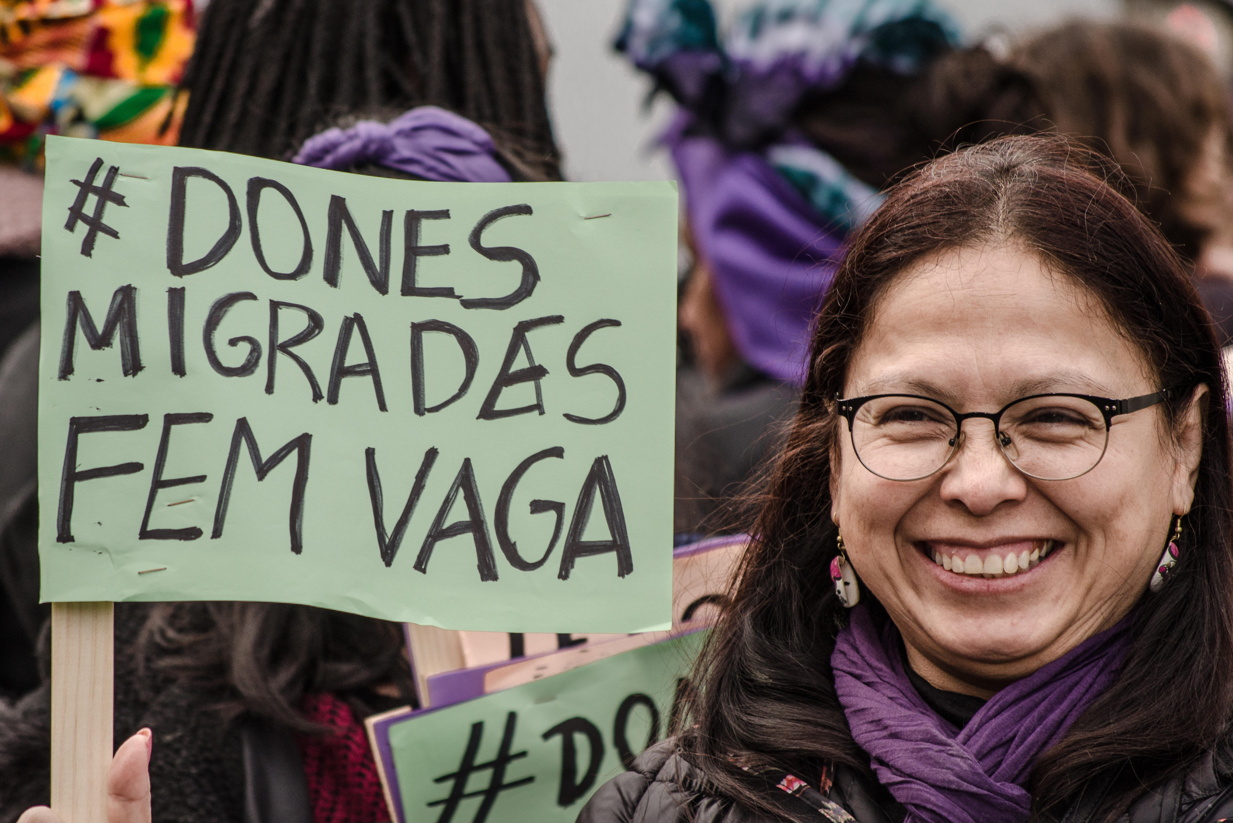 A protester seen displaying a poster relating to migrant women on strike. The Poster says 'Dones Migrades Fem vaga', 'Migrant women on the move'.