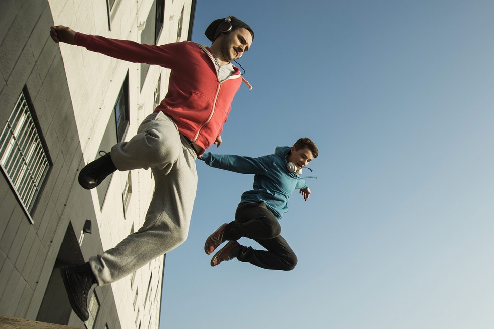 2 junge Männer springen dynamisch von einer Mauer