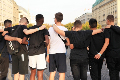 Jungen, die zu einer Sportmannschaft gehören, stehen gemeinsam am Brandenburger Tor, um Fotos zu machen. Einige von ihnen haben Migrationshintergrund, andere nicht. 