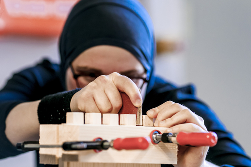 A refugee woman with a headscarf works in the training workshop for handicraft training.