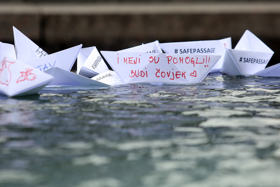 Beschriftete Papierschiffchen in einem Brunnen in Zagreb/Kroatien mit den Worten auf Kroatisch: "Mir haben sie geholfen: Sei ein Mensch!" und auf Englisch "Sichere Überfahrt".