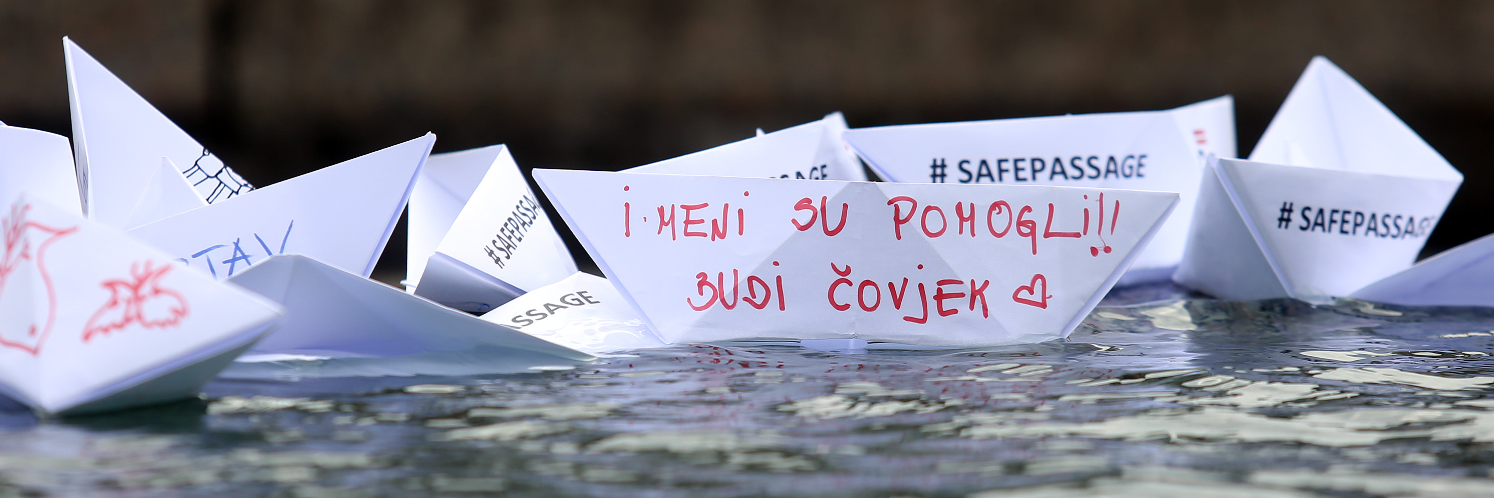 Paper boats in a fountain in Zagreb, Croatia, with the words in Croatian: ‘They helped me: Be human!’ and in English: ‘Safe passage’.