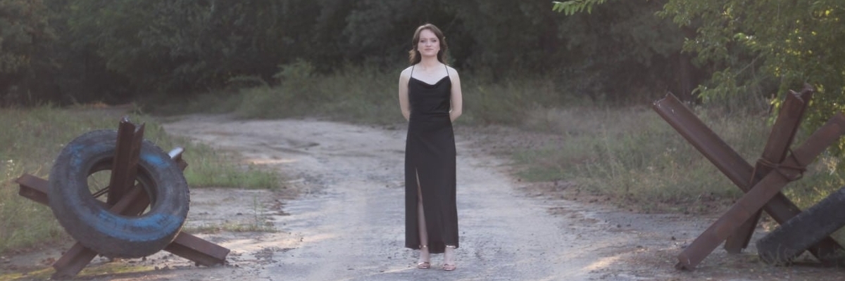 Iryna Pinchuk in a black evening dress in her home country of Ukraine next to border elements.