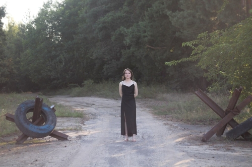 Iryna Pinchuk in einem schwarzen Abendkleid in ihrer Heimat der Ukraine neben zwei Panzersperren aus Stahl.