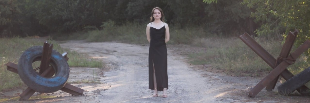 Iryna Pinchuk in a black evening dress in her home country of Ukraine next to border elements.