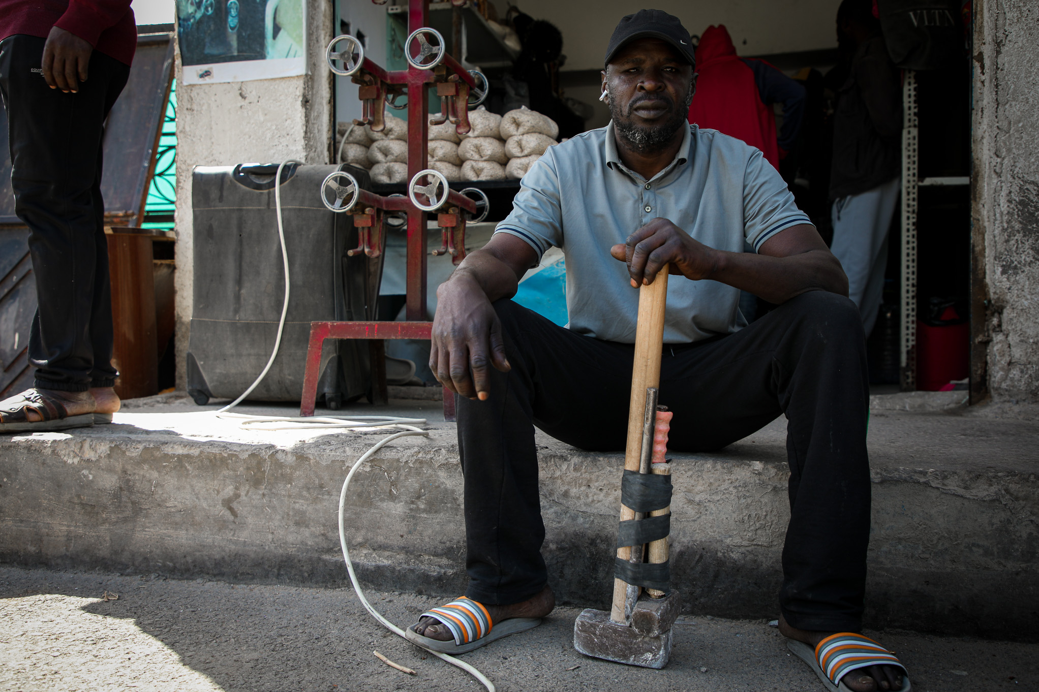 Ein Arbeitsmigrant sitzt in Tripolis/Libyen auf einer Schwelle mit einem Arbeitshammer in der Hand und schaut in die Kamera.