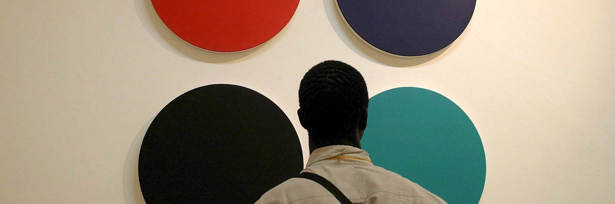 Ein Mann steht mit dem Rücken zur Kamera und schaut sich ein Gemälde mit vier verschiedenfarbigen Kreisen an.