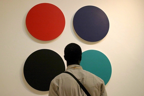Ein Mann steht mit dem Rücken zur Kamera und schaut sich ein Gemälde mit vier verschiedenfarbigen Kreisen an.