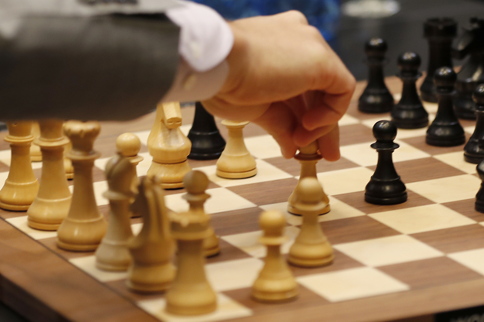 Schachbrett mit Figuren. Eine Hand bewegt einen weißen Bauern in Richtung schwarzes Spielfeld.