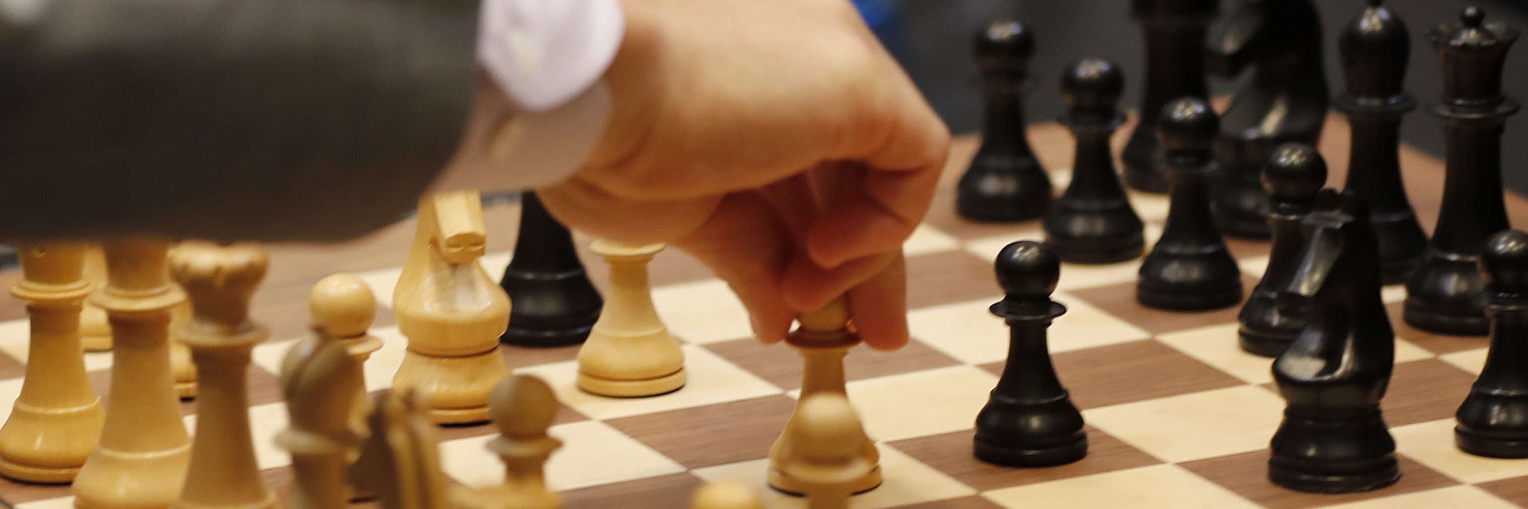 Chessboard with pieces. A hand moves a white pawn towards the black playing field.